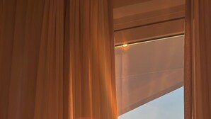 A room with a large window, curtains, and a view of the sunset.