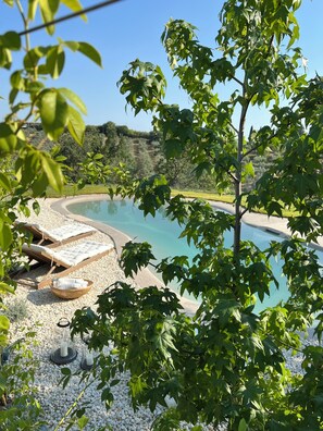 A poolside area with lounge chairs and a small table, surrounded by pebbles and greenery.