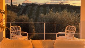A balcony with two white chairs and a sofa, overlooking a landscape with trees and a distant building.