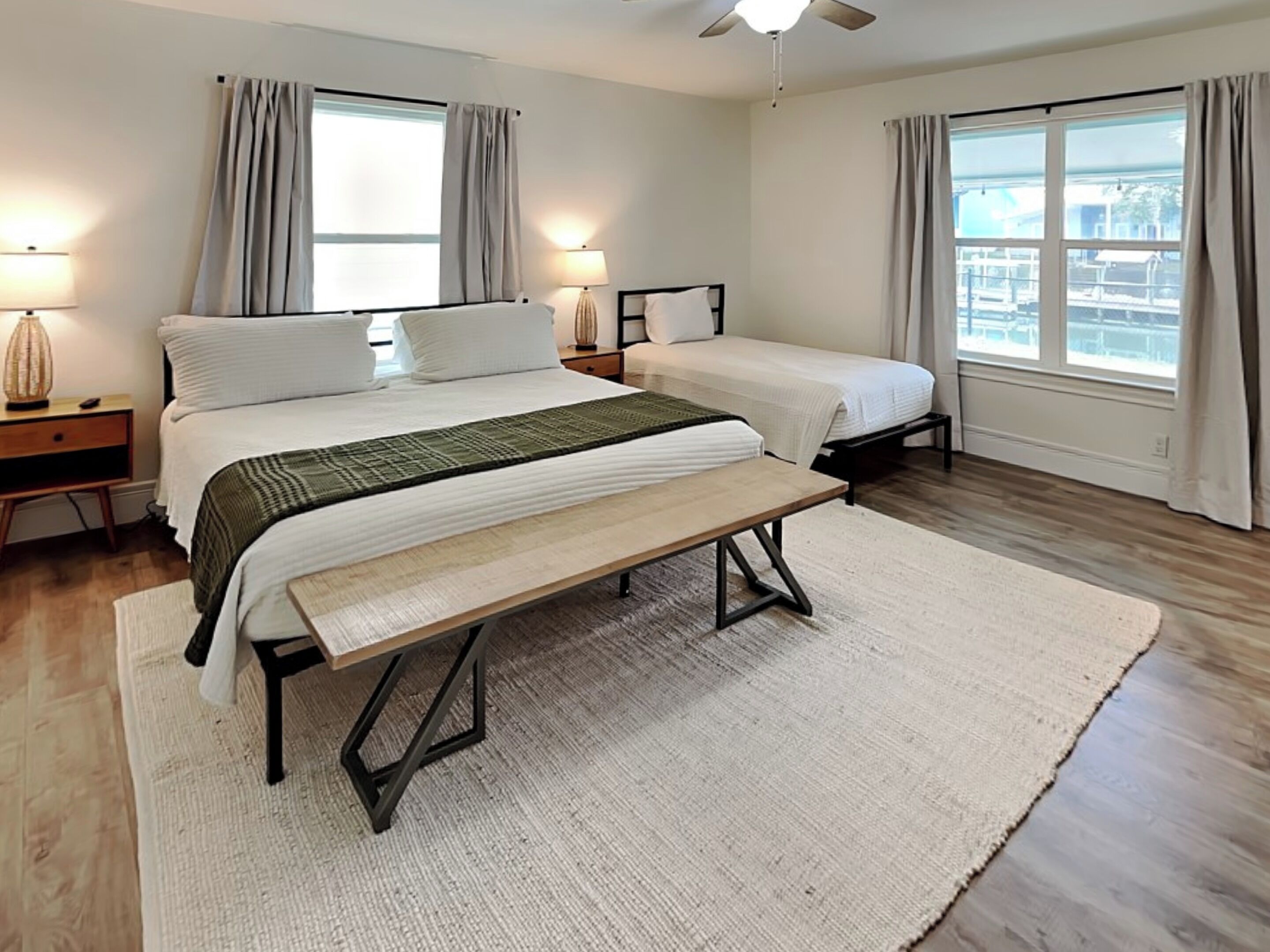 Ein Schlafzimmer mit zwei Betten, einer Bank und Blick auf die Stadt durch große Fenster.