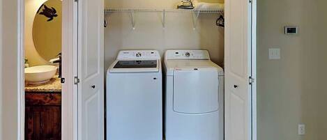 A laundry room with two white front-loading washing machines and a shelf above them.