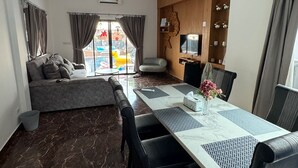 Una sala de estar moderna con un sofá, una mesa de comedor con sillas, un televisor y un mueble de madera con objetos decorativos.