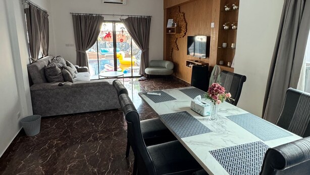Una sala de estar moderna con un sofá, una mesa de comedor con sillas, un televisor y un mueble de madera con objetos decorativos.