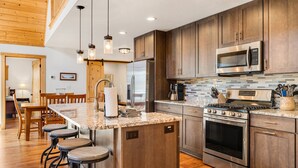 Una cocina moderna con gabinetes de madera, electrodomésticos de acero inoxidable, encimera de granito y taburetes de bar.