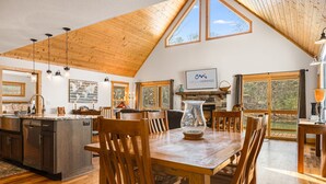 Una cocina amplia con techo de madera, un comedor con sillas de madera y un ventanal con vistas a un paisaje natural.