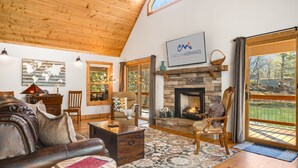 Una sala de estar acogedora con chimenea de piedra, sofá de cuero y un gran ventanal con vistas al exterior.