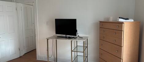 A bedroom with a bed, a desk with a TV, a dresser, and a door.