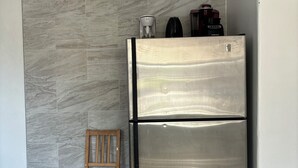 A kitchen with a stainless steel refrigerator, a wooden chair, and a marble-patterned wall.