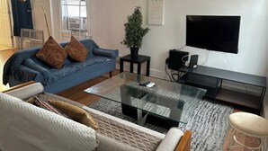A living room with a blue sofa, a glass coffee table, a television, and a potted plant.