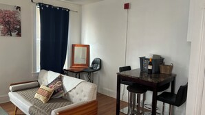 A living room with a sofa, a dining table with chairs, a mirror, and a ceiling fan.