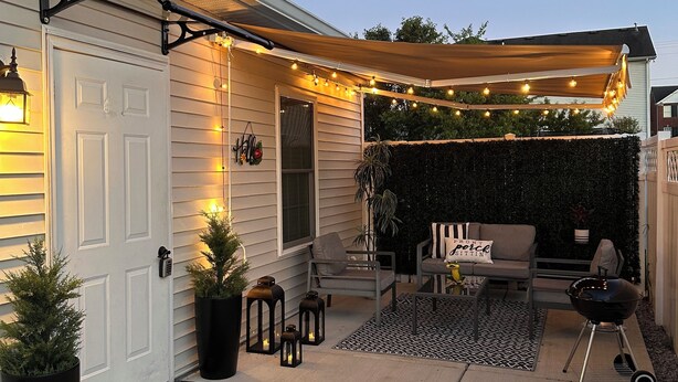 A covered patio area with string lights, outdoor furniture, and a grill.