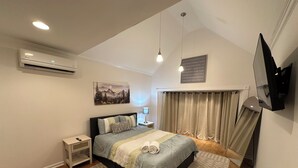 A modern bedroom with a bed, bedside tables, a mounted TV, and a large window with curtains.