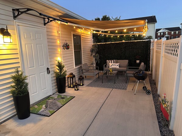 Eine überdachte Terrasse mit Lichterketten, Gartenmöbeln und einem Grill.