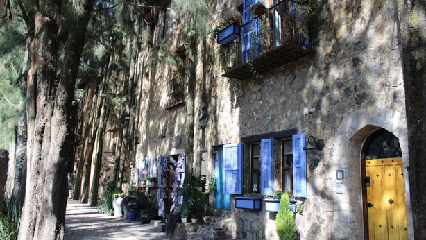 A stone building with blue shutters and a yellow door, surrounded by trees.