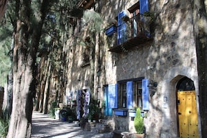 Un edificio de piedra con contraventanas azules y una puerta amarilla, rodeado de árboles.