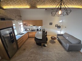 Una cocina moderna con horno empotrado, microondas y estufa a gas. Hay un comedor con mesa y sillas, y un sofá gris en la sala.