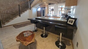 A modern kitchen with a central island, bar stools, a wooden coffee table, and a staircase.