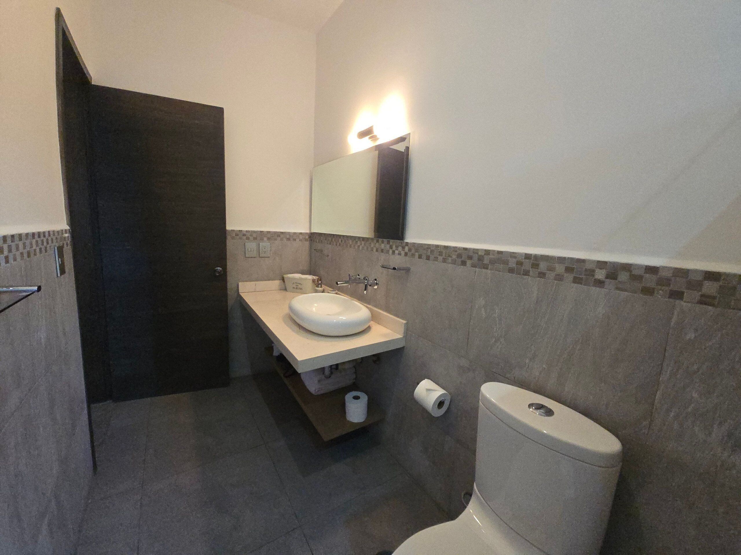 A bathroom with a toilet, sink, mirror, and a roll of toilet paper.