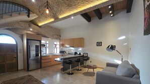 A modern kitchen with a built-in refrigerator, a dining area with a bar stool, a gray sofa, and a patterned rug.