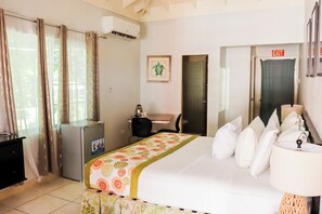 A hotel room with a bed, a desk, a chair, an air conditioner, and an exit sign. - Paradise on the Rocks - Suite W/Balcony & Sea Views #5 (Negril)