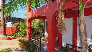 Un edificio rojo con una puerta blanca, una escalera y un pequeño jardín con plantas y un banco.