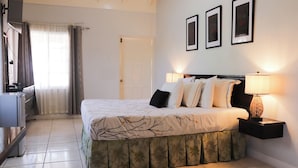 A neatly arranged bedroom with a bed, bedside lamps, and a door. - Paradise on the Rocks - Suite w/Kitchenette #9 (Negril)