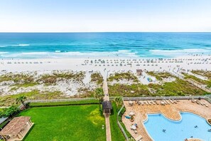 Vista aérea de um resort à beira-mar, com piscina, área de praia e gramado.