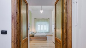 Een slaapkamer met een houten vloer, een bed, een raam met gordijnen en een hanglamp.