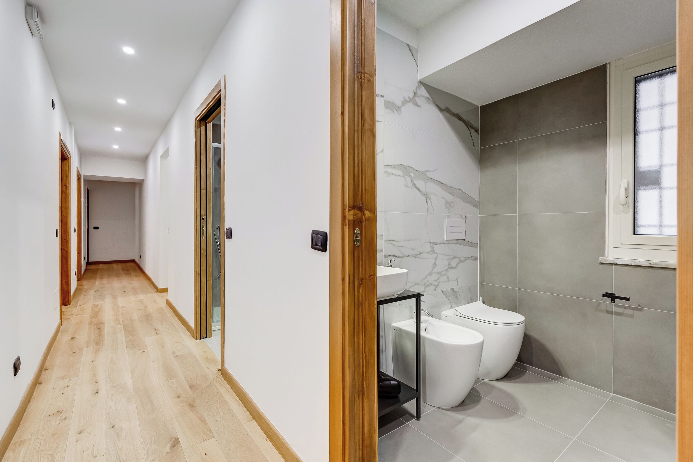 Un bany modern amb una paret de marbre, un vàter i un lavabo.