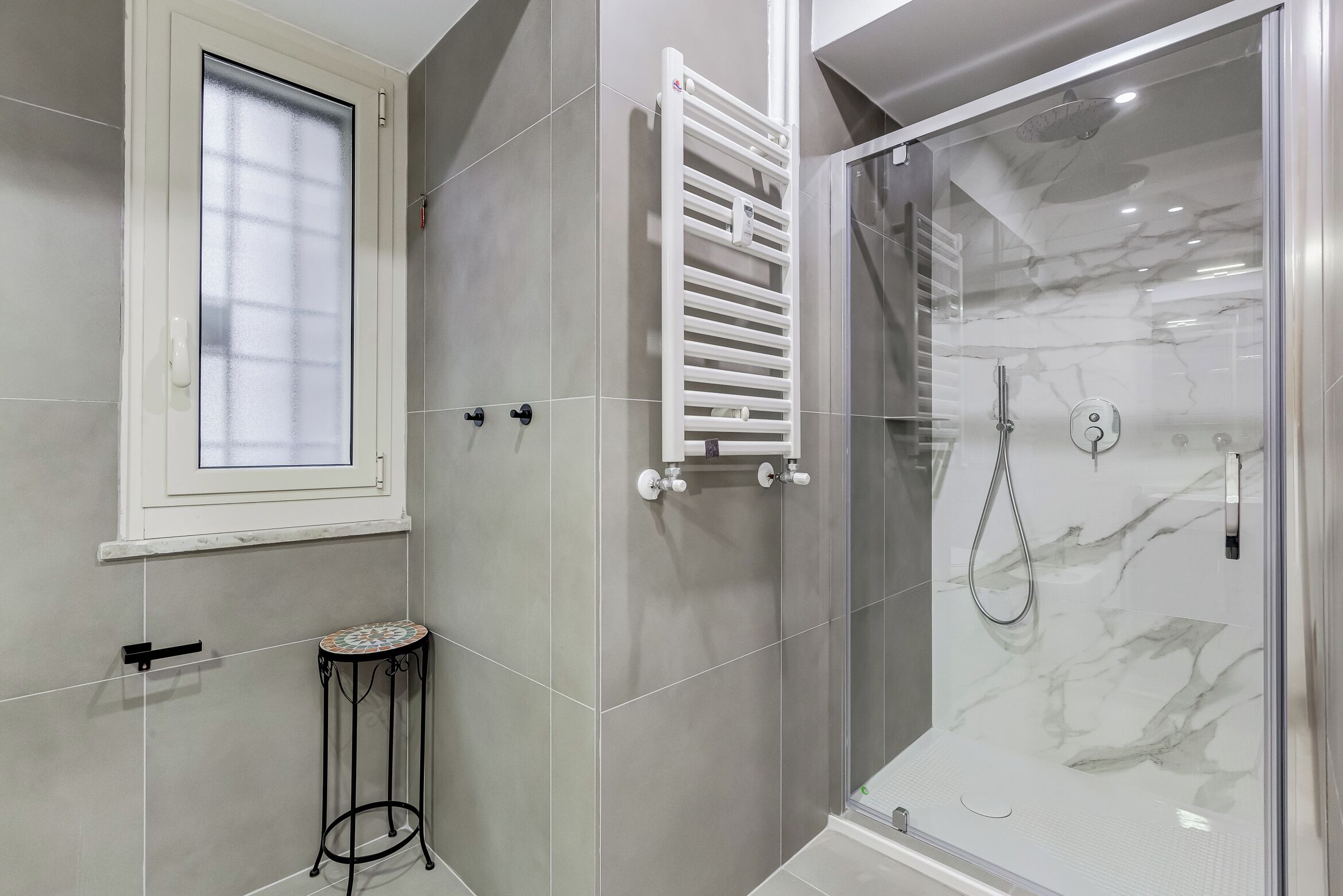 Une salle de bain moderne avec une douche à parois de verre, un porte-serviettes blanc et une petite table ronde.