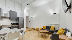 Een moderne keuken met witte kasten, een eettafel met stoelen, en een zithoek met een bank en poefs.