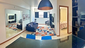 Una sala de estar moderna con un sofá, una mesa de centro y un televisor. Hay una alfombra estampada en el suelo y un espejo grande en la pared.