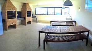 A room with two brick-built barbecue ovens, a large window with a city view, and a table with benches.