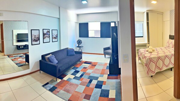 Una sala moderna con un sofá, televisión, cuadros enmarcados y una alfombra colorida.