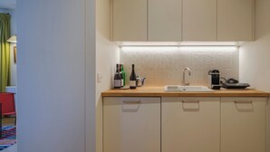 Una cocina compacta con un lavamanos, una cafetera y botellas de vino.