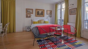 Un dormitorio con una cama, dos sillas, una mesita, un ventilador y una alfombra colorida.