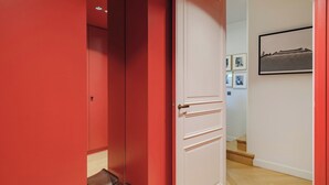 Un pasillo con una puerta roja, una blanca y una escalera que sube a otra habitación.