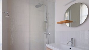 Un baño moderno con cabina de ducha de vidrio, un espejo redondo y un lavamanos blanco con repisa de madera.