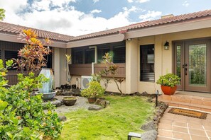 A residential building with a tiled roof, a front door with a glass panel, and a small garden with various plants and a water feature. - Luxury Home w/Pool, King Suites & Sunset Views (Kailua-Kona)