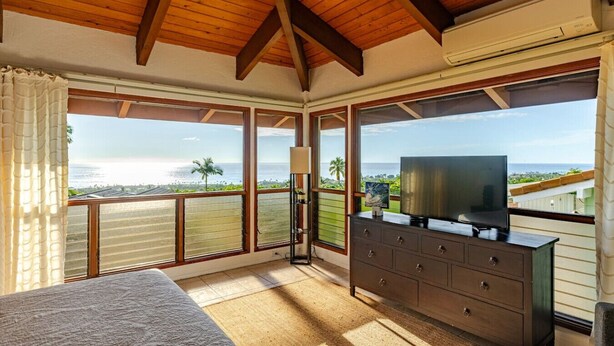 A bedroom with a large window, a television on a dresser, and a ceiling fan.