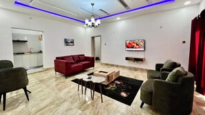 Una sala de estar moderna con un sofá rojo, un televisor montado en la pared y una cocina visible a través de una puerta abierta.