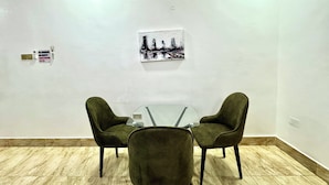 Una habitación con una mesa de vidrio y dos sillas verdes, un cuadro en la pared y un cartel de prohibido fumar.