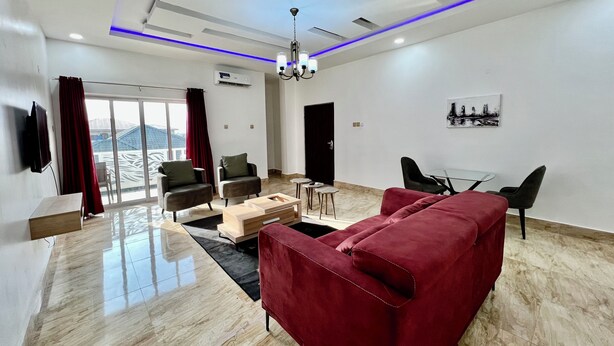 Una sala de estar moderna con un sofá rojo, dos sillones, una mesa de centro de vidrio y un comedor con una mesa pequeña y sillas.