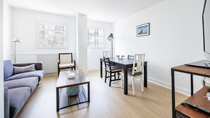 Ett modernt vardagsrum med en grå soffa, ett soffbord, ett matbord med stolar och en tv-apparat placerad på ett träställ.