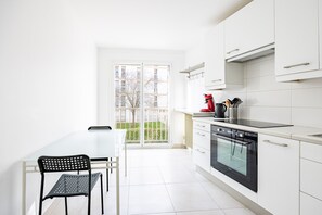 A modern kitchen with white cabinets, a black oven, and a dining area with a white table and black chairs. - L’Écrin Franklin - Proche Château de Versailles (Versailles)