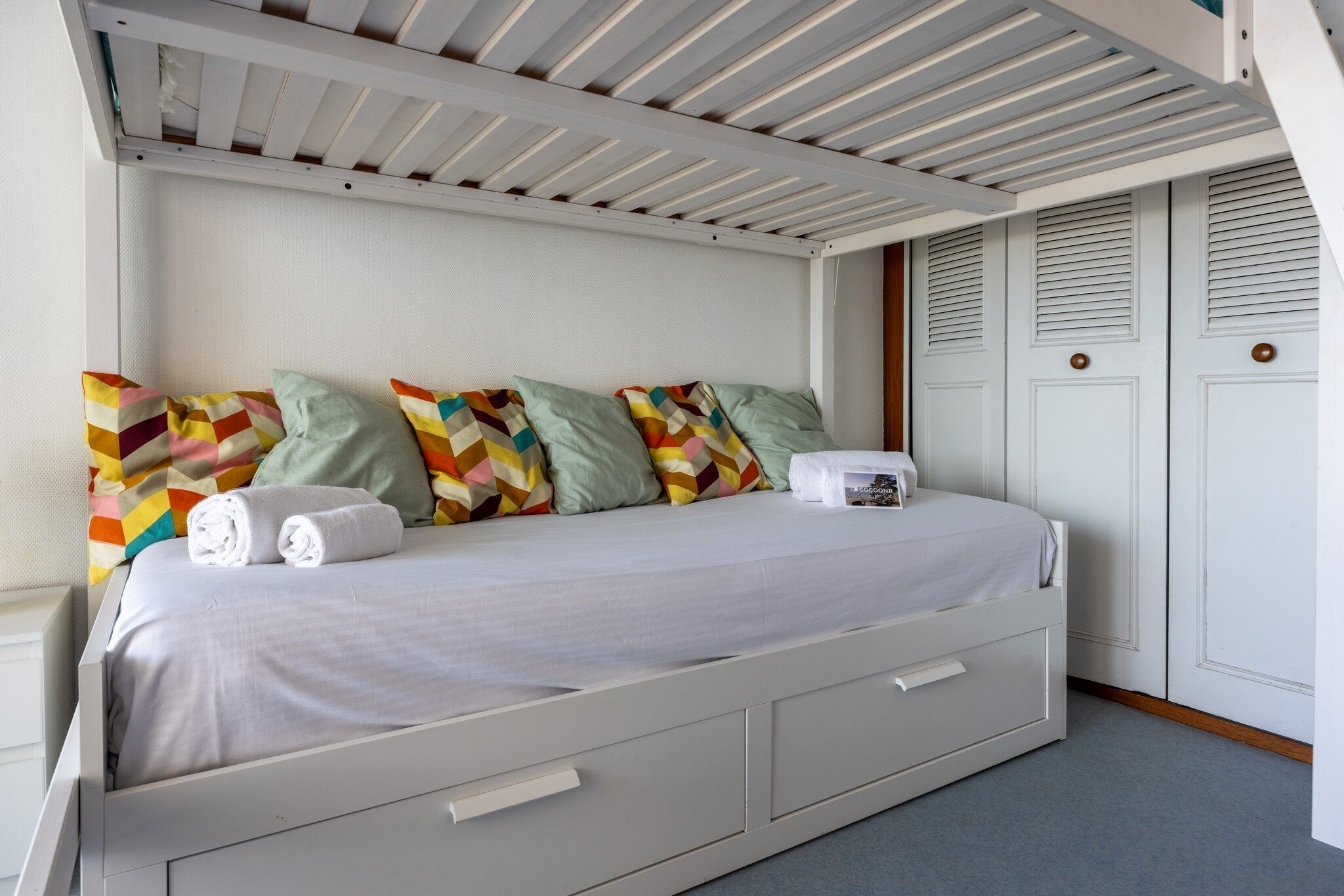 A neatly made bed with a white headboard, multiple pillows, and a pair of folded towels.