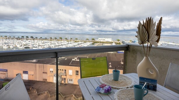 A balcony with a view of a marina, a table with a vase and a book, and a chair. - Horizon Bleu - Superbe vue sur le port (Arcachon)