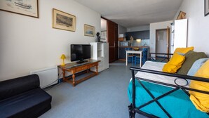 A compact living space with a sofa, a bed with colorful bedding, a television, and a small kitchen area. - Horizon Bleu - Superbe vue sur le port (Arcachon)