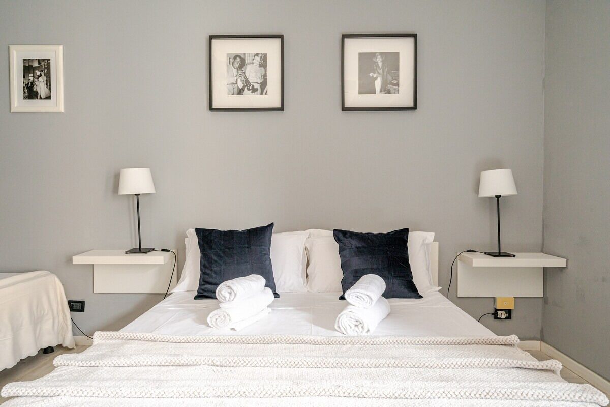 A hotel room with a neatly made bed, two bedside tables with lamps, and three framed pictures on the wall.
