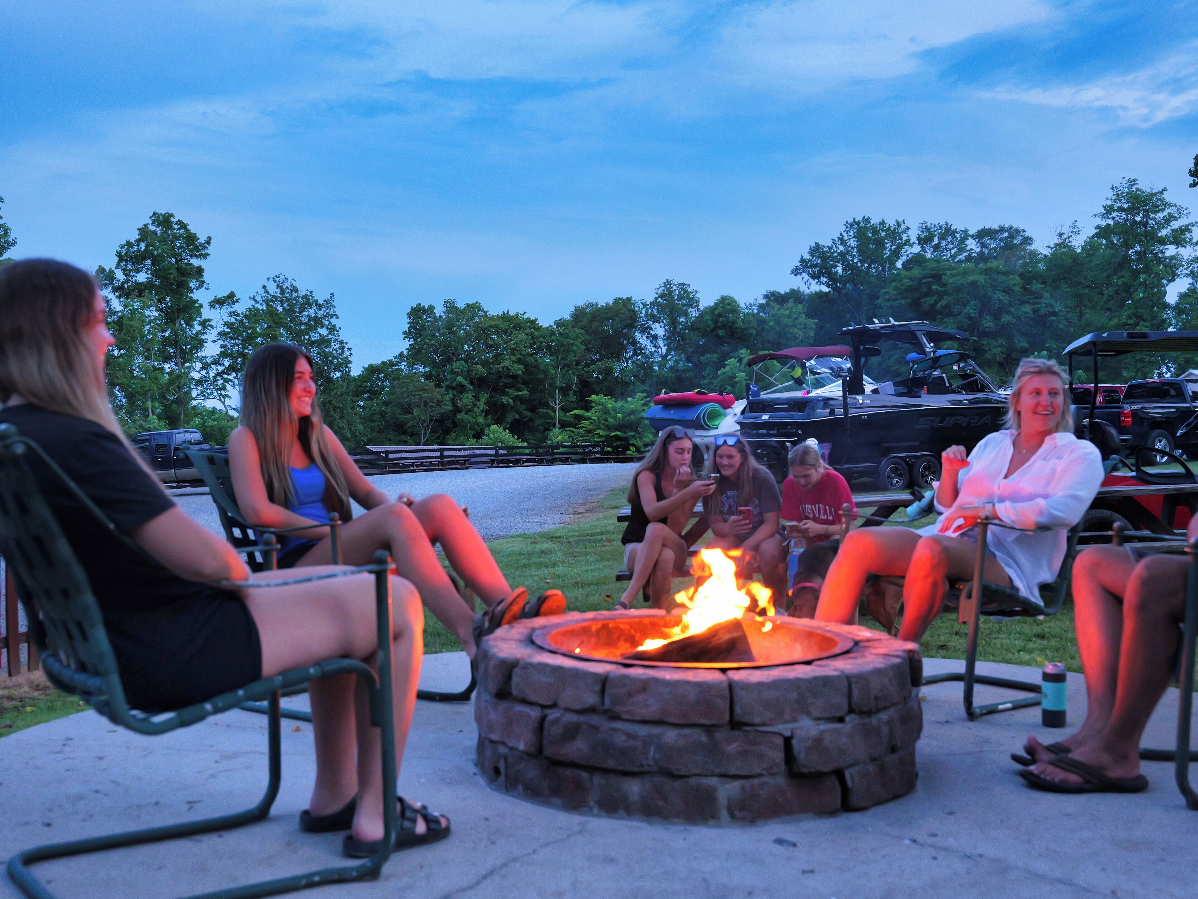 A group of people sitting around a stone fire pit in an outdoor setting.